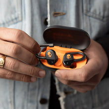 Orange charging case with black earbuds being inserted by hands