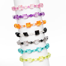 Stacked beaded bracelets on a wrist stand, pink, purple, orange, black, clear, teal, and yellow-green