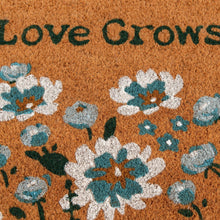 Close-up outdoor doormat showing 'Love Grows Here' text and blue blossoms