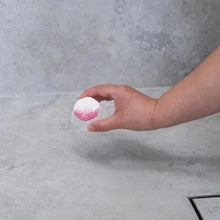 Shower steamer in hand, white tablet with pink swirl, over shower floor
