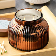 Amber ribbed glass jar candle with wooden lid and lit wicks