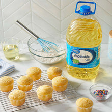 Vegetable oil bottle beside frosted muffins on a cooling rack and small bowls.