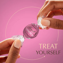 Hands unwrapping a LINDOR Strawberries & Cream chocolate truffle