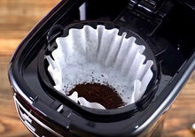 Black drip coffee maker filter basket with paper liner and coffee grounds