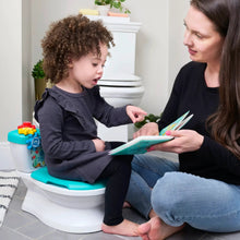 Toddler sitting on a teal potty training seat while adult reads