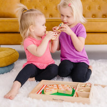 Two toddlers playing with a wooden pizza set and topping pieces