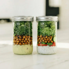 Clear wide-mouth glass mason jar with metal lid, filled with vegetables and herbs