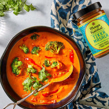 Tikka masala simmer sauce jar next to a bowl of orange curry with broccoli