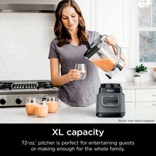 Dark gray blender on kitchen counter with clear pitcher pouring blended orange drink