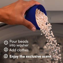Laundry scent booster beads pouring into washer with blue scoop and white beads