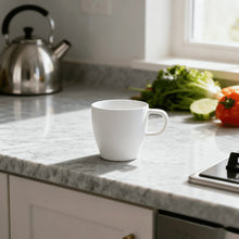 White coffee mug with curved handle on a kitchen countertop.