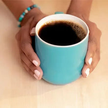 Turquoise mug with dark coffee held in hands, white rim