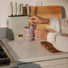 Purple floral stoneware mug held while pouring from a utensil