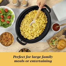 Black oval slow cooker insert filled with cooked macaroni with serving spoon