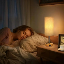 Touch table lamp with cream fabric shade and wood base glowing beside bed