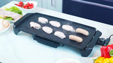 Electric griddle cooking surface with raw chicken and sausages on non-stick plate