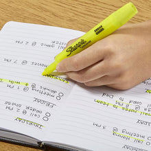 Hand using yellow tank-style highlighter with chisel tip on notebook pages