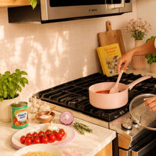 Pink ceramic non-stick saucepan on stove with wooden spoon stirring contents