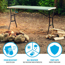 Gray folding rectangle table with black legs outdoors near rocks and fire pit area.