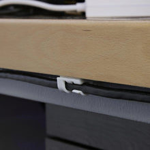 White cable clip attached to a surface edge, holding a black cable in place.