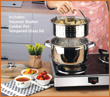 Stainless steel steamer pot with perforated basket and glass lid on stovetop.