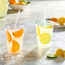 Clear disposable plastic coffee cups with lids and white straws, citrus fruit pieces