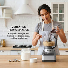 Gray food processor on countertop with clear bowl containing blended mixture and lid