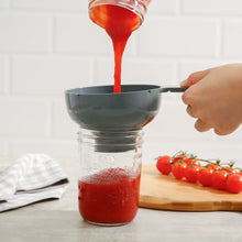 Canning funnel pouring red liquid into a glass canning jar