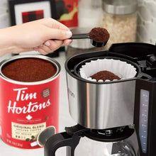 Tim Hortons Original Blend ground coffee scoop near red can and coffee filter brewer.