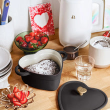 Black heart-shaped Dutch oven with lid open and gold knob on tabletop