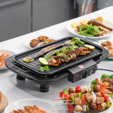 Electric smokeless grill with fish and vegetables on the cooking plate, black base.