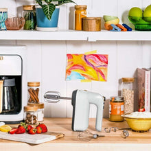 White electric hand mixer with beaters, dough hooks, and storage case on countertop