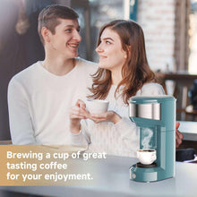 Teal single-serve coffee maker brewing steaming coffee held by two people
