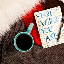 Coffee mug with dark brew beside other packaging on textured blanket