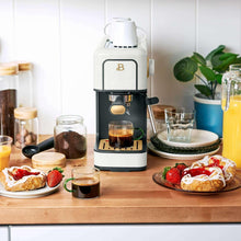 White espresso machine on countertop with espresso cup, milk jug, and pastries nearby
