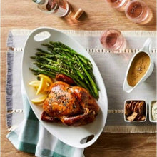 White oval porcelain serving tray with side handles holding roasted chicken and asparagus
