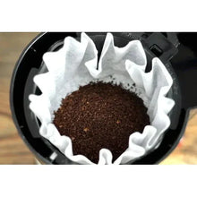 Coffee maker brew basket with white paper filter filled with ground coffee