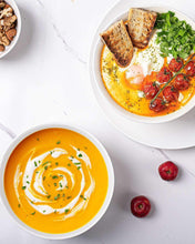 White ceramic dipping bowls filled with yellow soup, bread, and greens