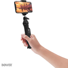 Hand gripping the wireless remote on a black selfie tripod with smartphone mount
