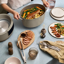 Beige multi-cooker with open lid, hands adding food to the cooking pot