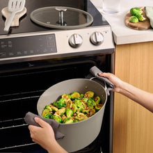 Beige multi-cooker base with open lid and digital display, hands placing pot into unit