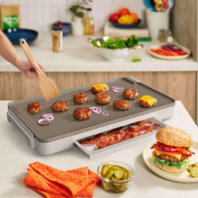Electric griddle with warming tray, open side tray with cooked food and burgers.