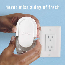 Hand holding white Febreze plug-in air freshener oil refill module with outlet prongs
