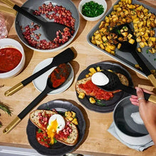 Black silicone kitchen utensils, including spatula and spoon, beside cookware