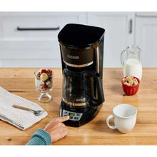 Black drip coffee maker on countertop with mug and glass serving items nearby