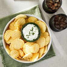 Wavy potato chips in a bowl with white dip and chopped herbs