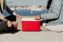 Red 9 qt cooler with white lid held by hands, lid closed