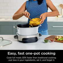 Multi-cooker on countertop with open pot while person adds ingredients