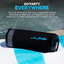 Black portable speaker with blue accent logo and side port, laid horizontally on a towel.
