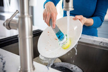 Dish scrub sponge refill on a wand rinsed under tap water while washing dishes